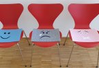 Three red chairs with blue, gray, and pink mats displaying happy, sad, and silent faces.